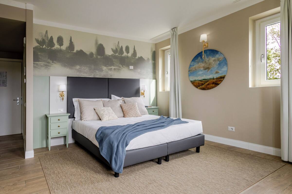 Une chambre à coucher comprenant un lit, des tables de chevet, une fresque murale, une fenêtre et une porte.