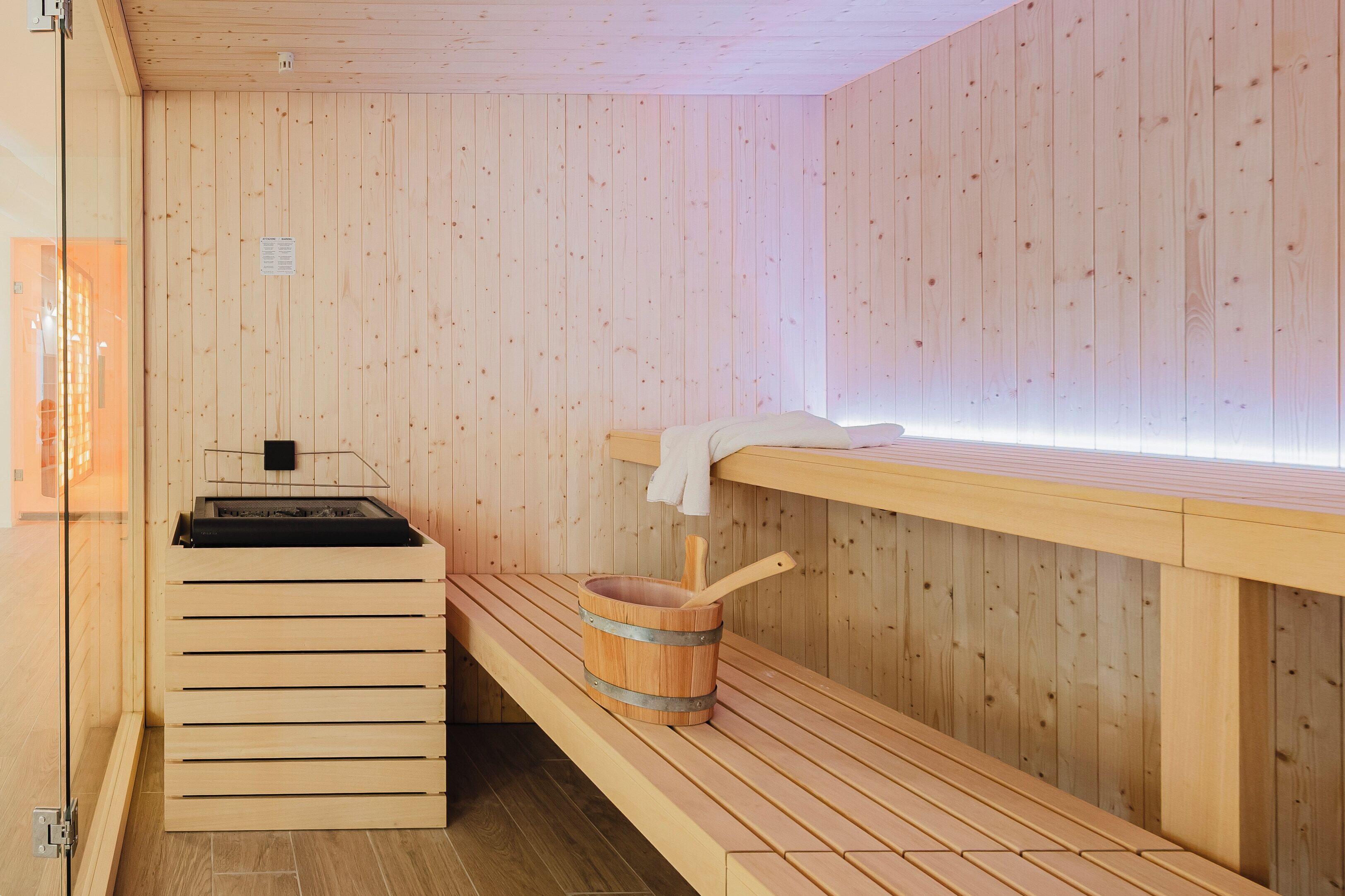 A sauna room with wooden benches, a wooden bucket, and a bench with a towel.