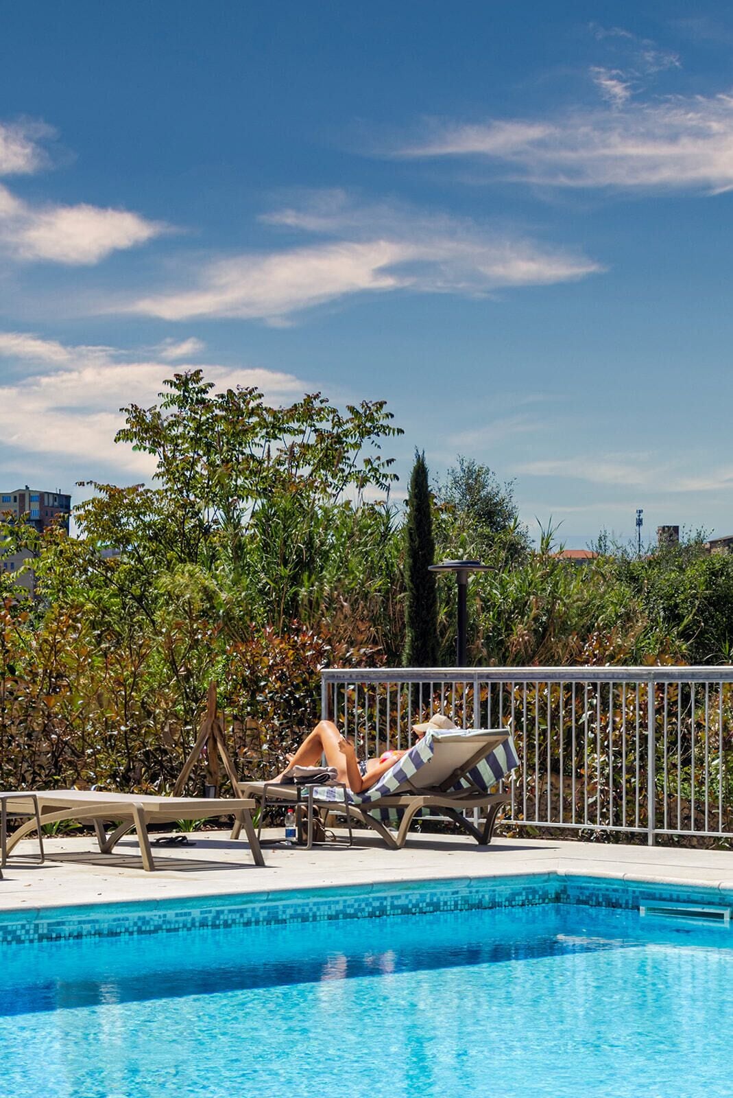 A swimming pool with lounge chairs, a metal fence, and greenery in the background.