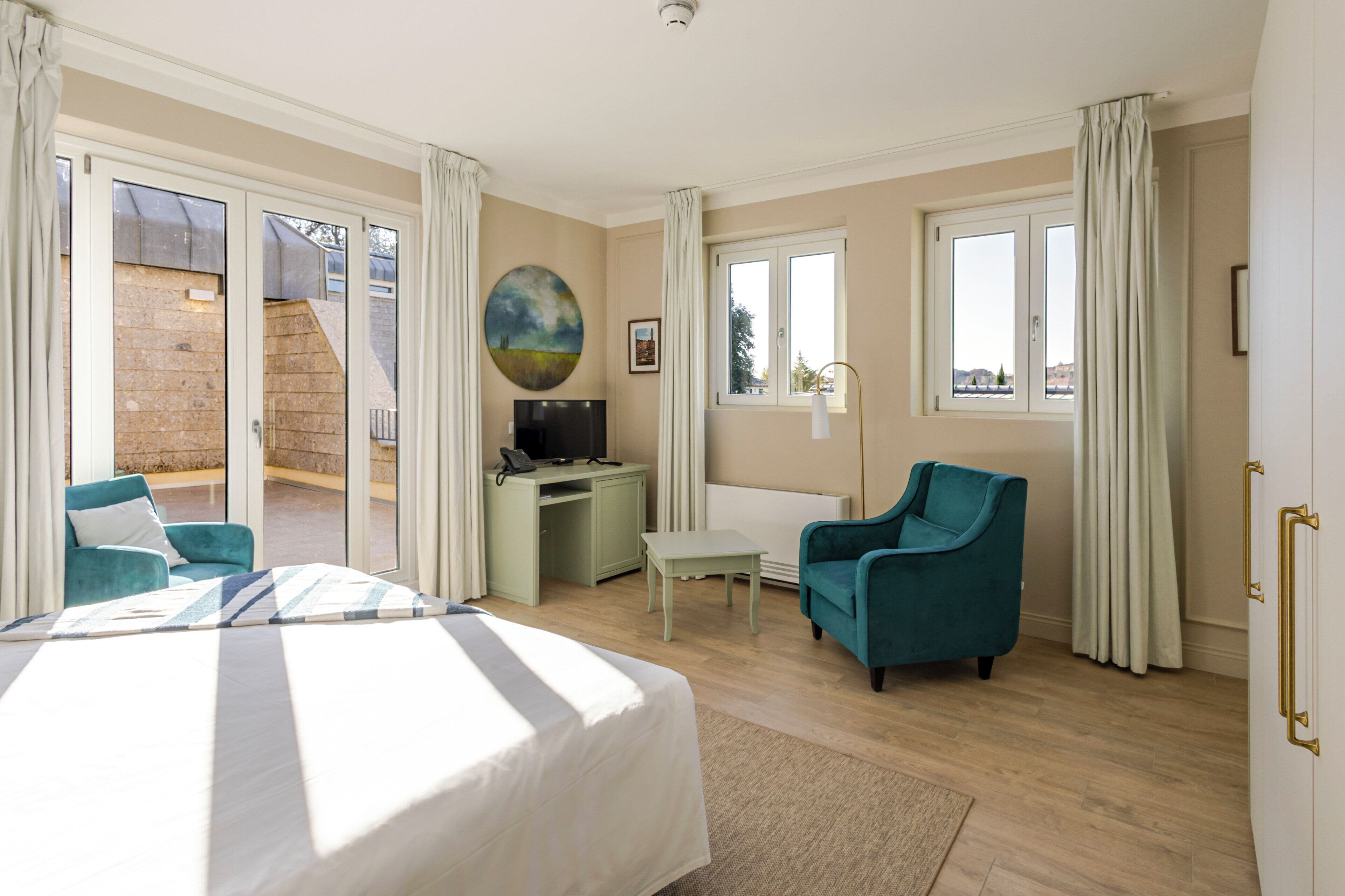 A bedroom with a bed, a desk, a chair, and a view of the outside.