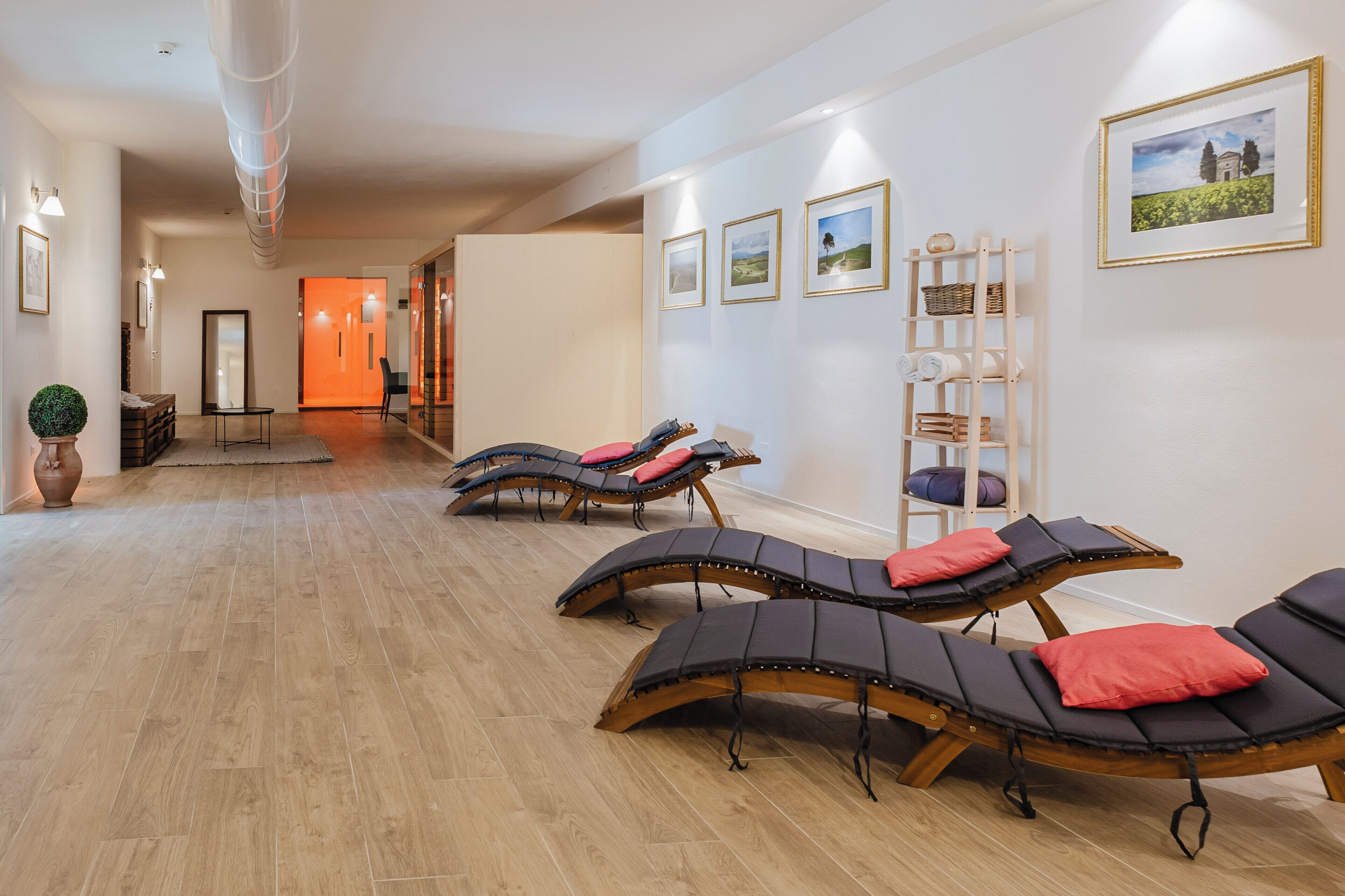 Une salle de spa avec un plancher en bois, des chaises longues, une étagère en bois en forme d’échelle et des tableaux encadrés au mur.