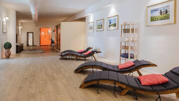 Une salle de spa avec un plancher en bois, des chaises longues, une étagère en bois en forme d’échelle et des tableaux encadrés au mur.