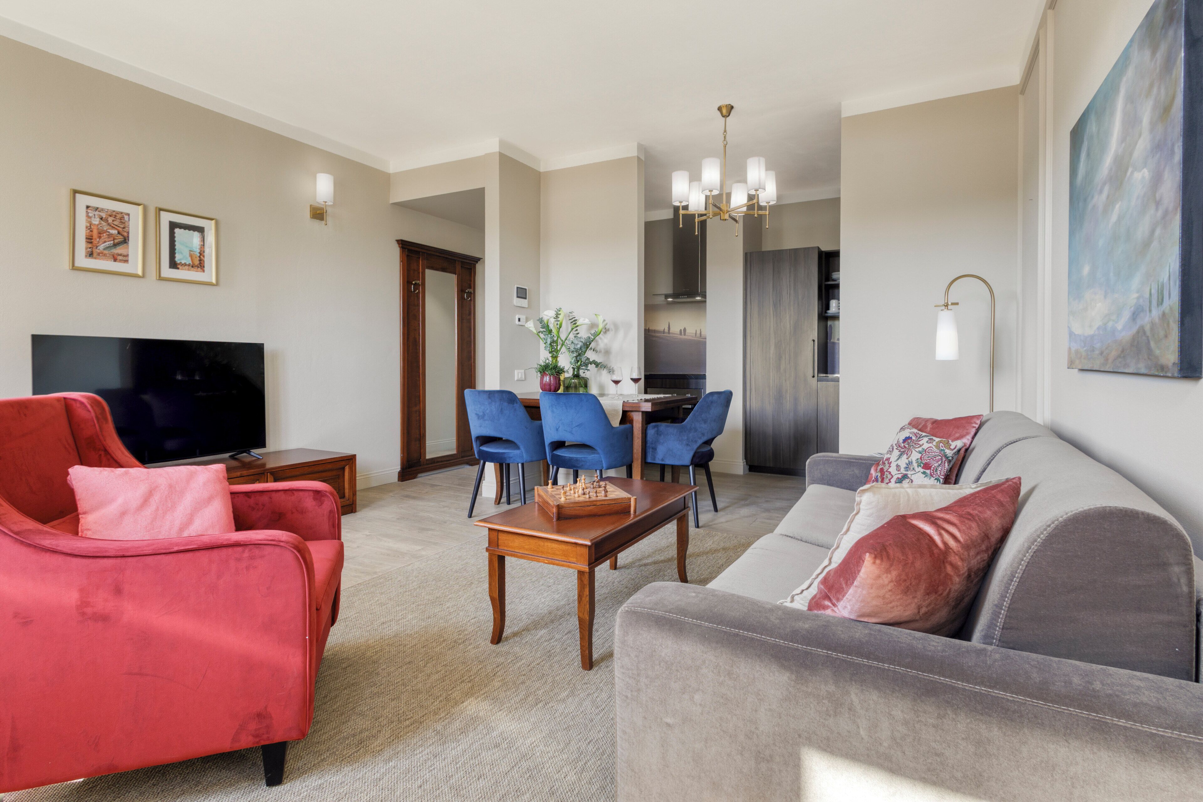 A living room with a red sofa, a grey sofa, a wooden coffee table, and a dining area with blue chairs.