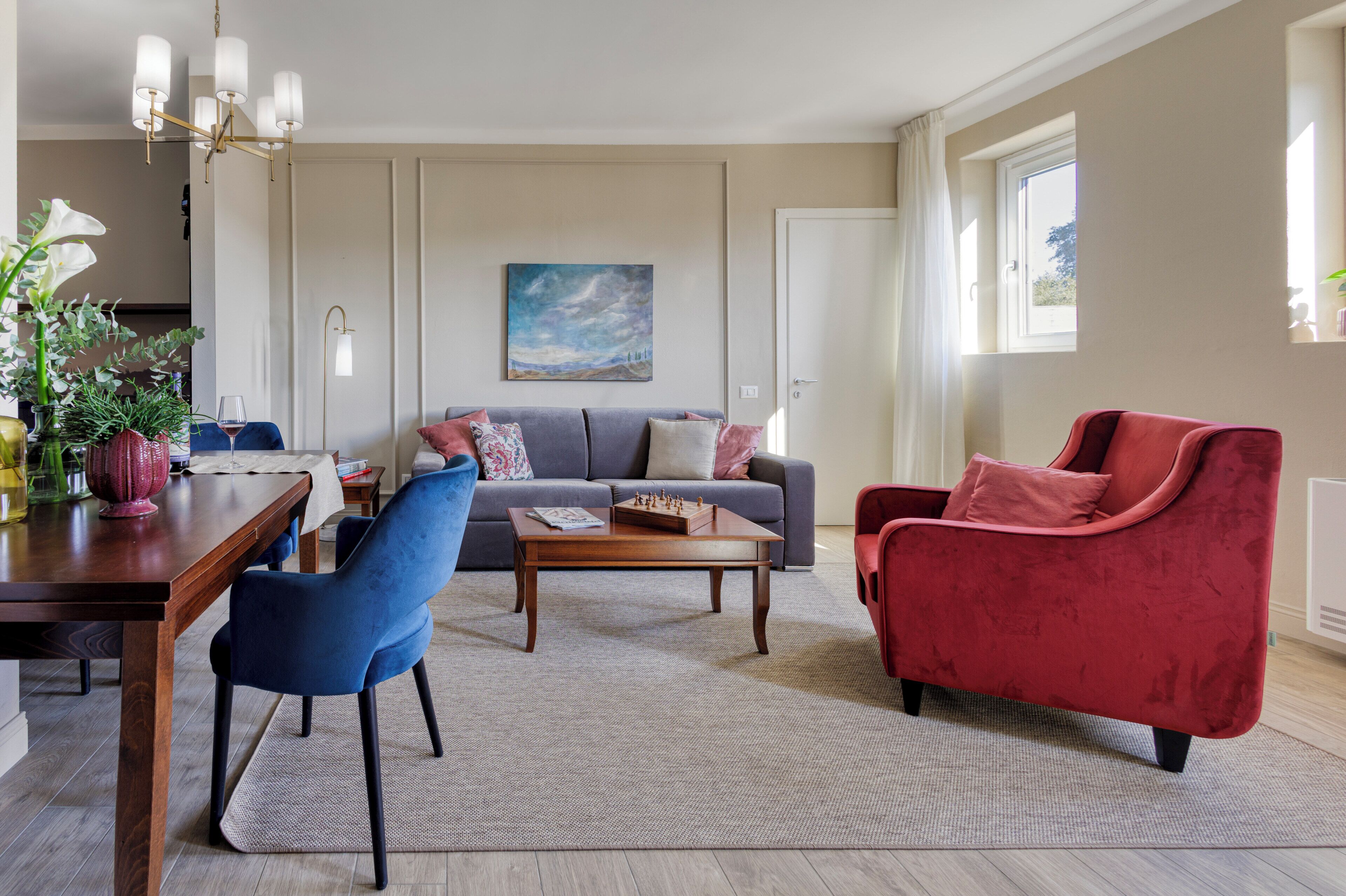 A living room with a sofa, a red armchair, a coffee table, and a dining area with a table and chairs.