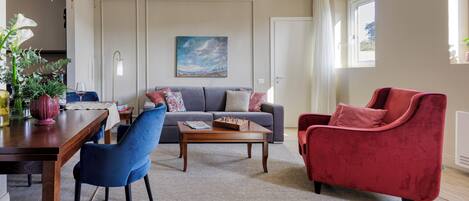 A living room with a sofa, a red armchair, a coffee table, and a dining area with a table and chairs.