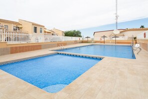 Una piscina con valla blanca, una silla de salvavidas y una sombrilla junto a la piscina.
