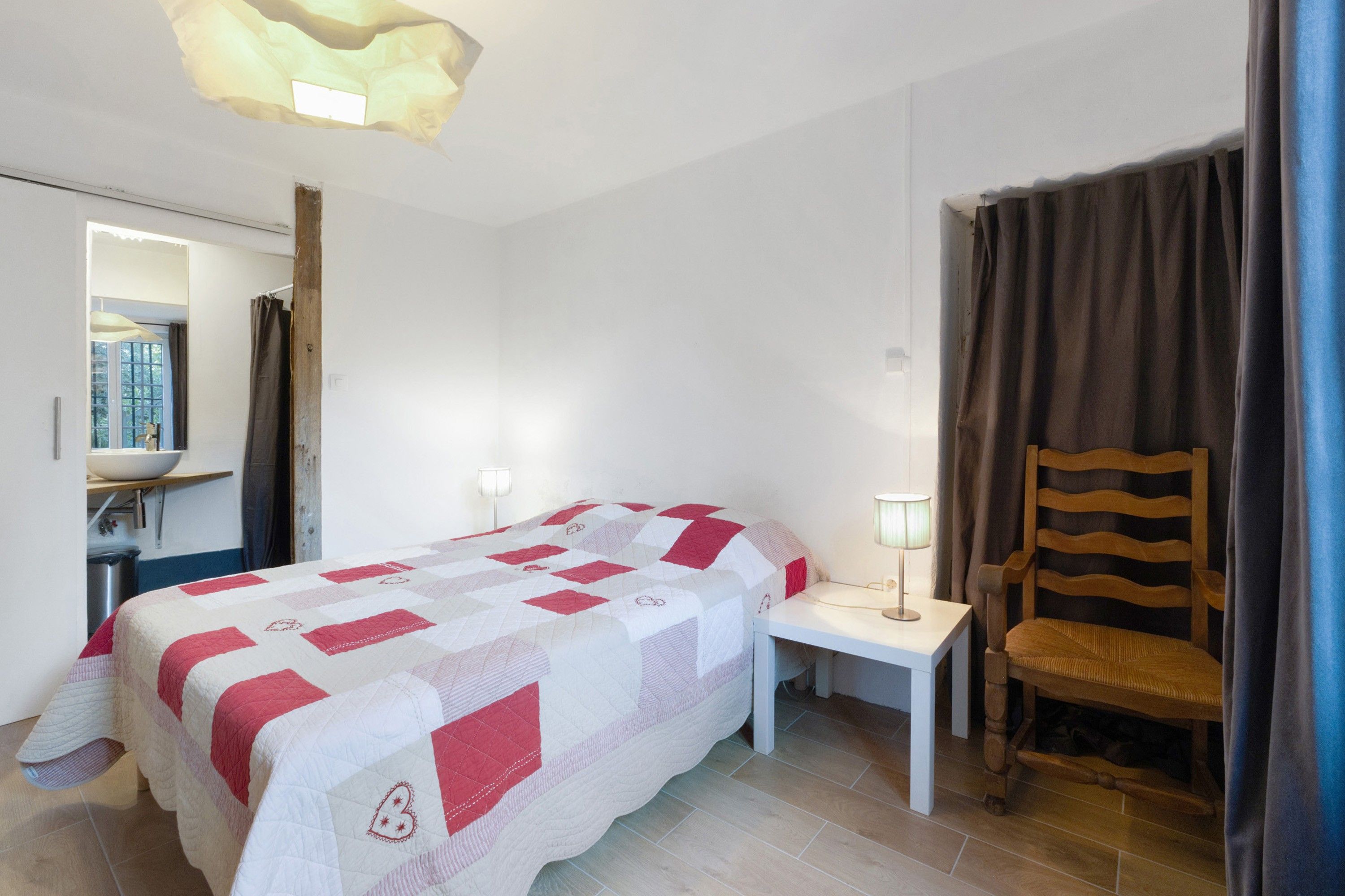 Een slaapkamer met een bed, nachtkastje, stoel en een spiegel.