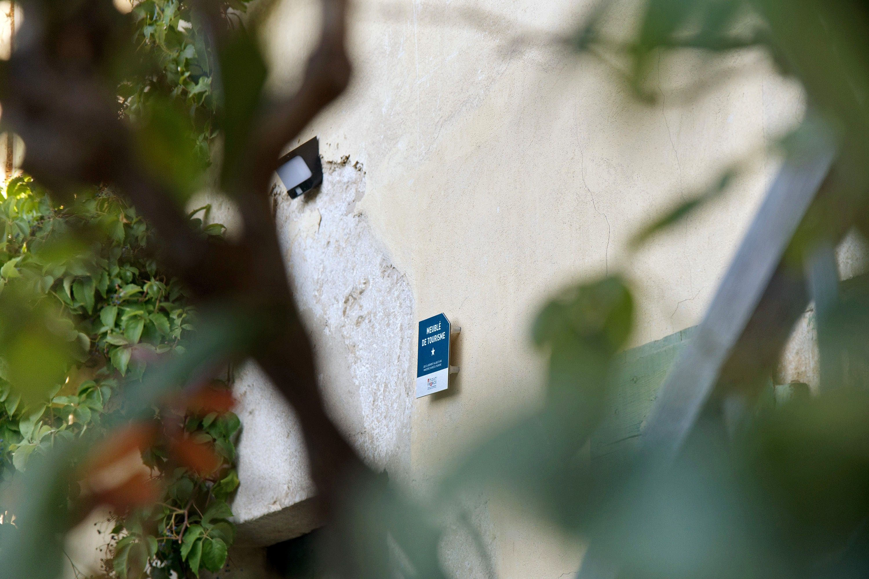 A wall with a blue sign that reads 'MEUBLE DE TOURISME' and a small, dark object attached to the wall.