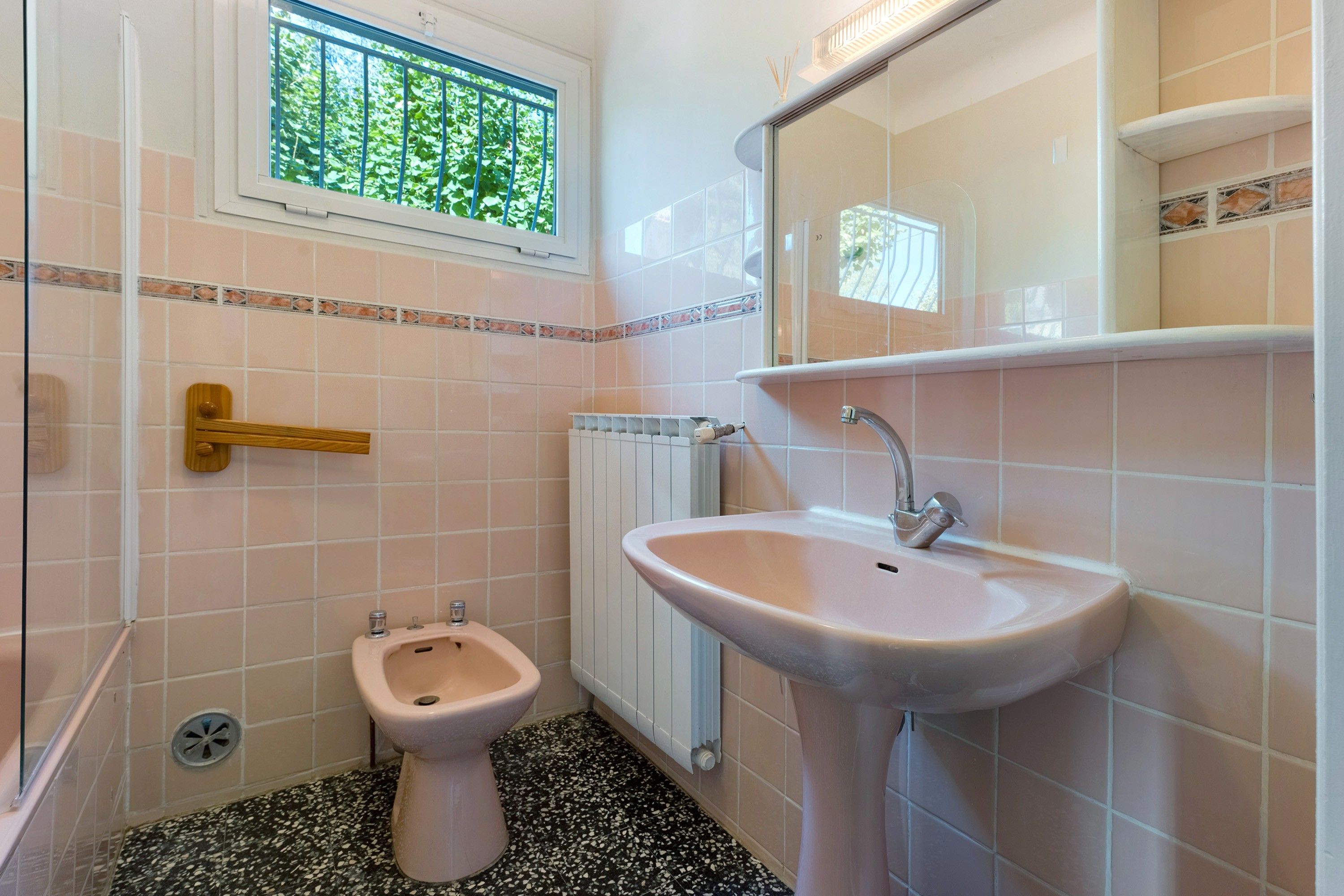 Ein kleines Badezimmer mit Toilette, Bidet und Waschbecken. Ein Fenster bietet Blick auf Grünfläche.