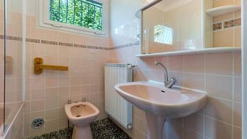 Ein kleines Badezimmer mit Toilette, Bidet und Waschbecken. Ein Fenster bietet Blick auf Grünfläche.