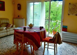 Ein Essbereich mit Tisch, Stühlen, einem Teekessel und einem Fenster mit Blick ins Grüne.