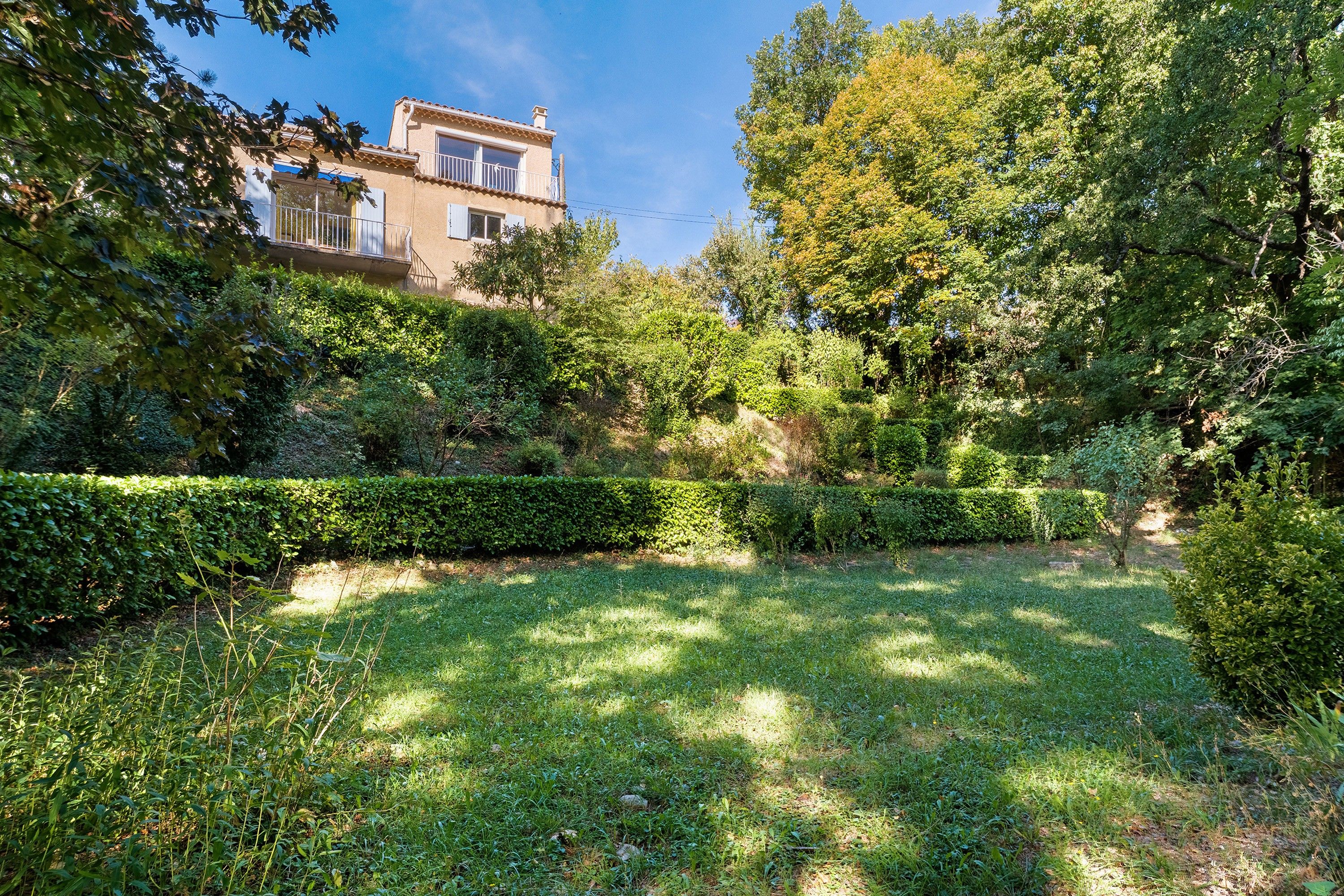 Ein gepflegter Garten mit Rasenflächen, Hecken und einem Gebäude mit Balkon.