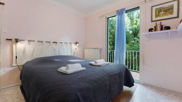 A bedroom with a large bed, a radiator, a window with curtains, and a balcony with a railing.