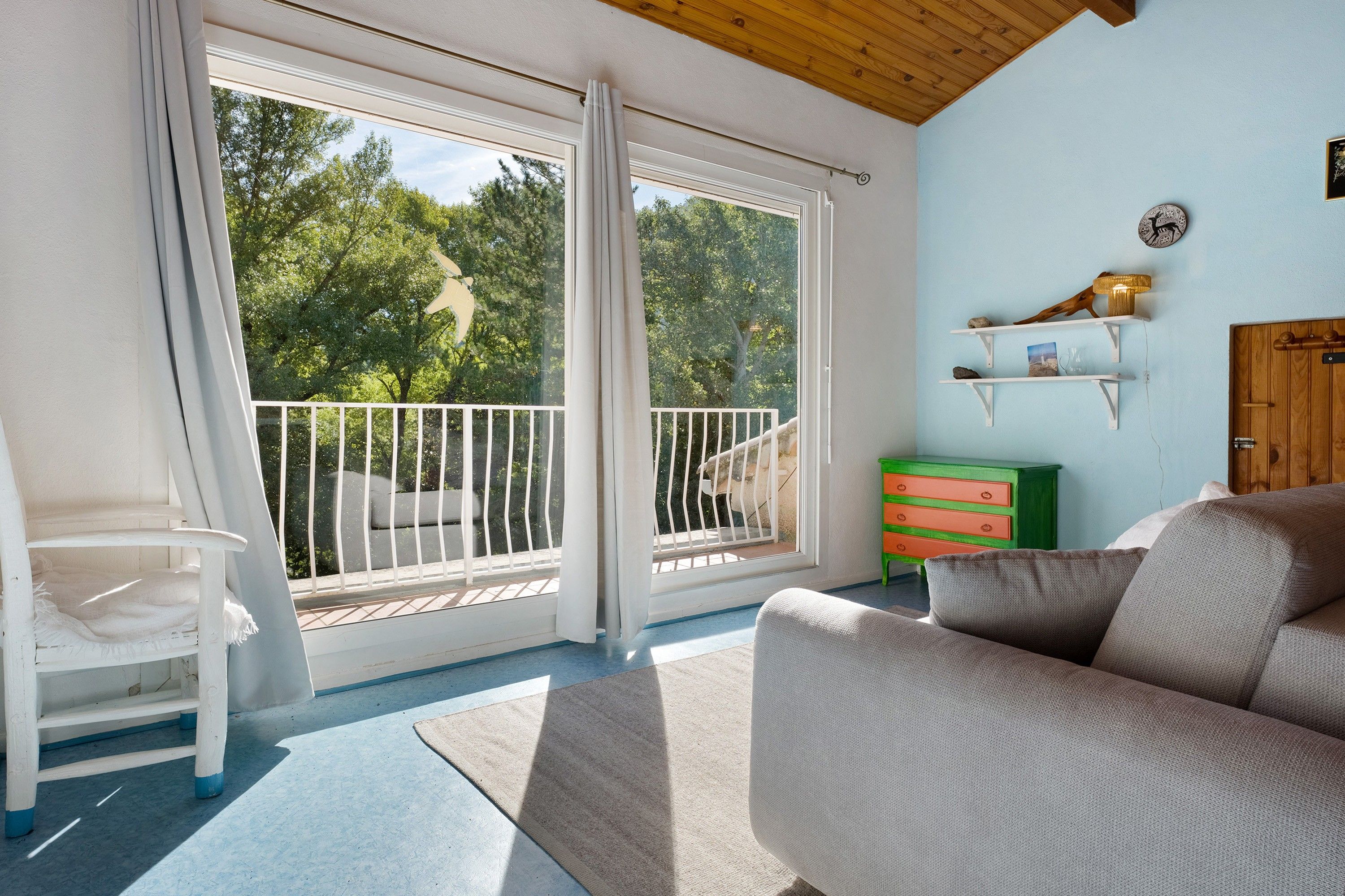 A room with a balcony, a white chair, a sofa, and a green dresser.