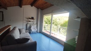 Ein Zimmer mit blauem Boden, einem grauen Sofa, einem weißen Heizkörper und einem Balkon mit weißer Brüstung.