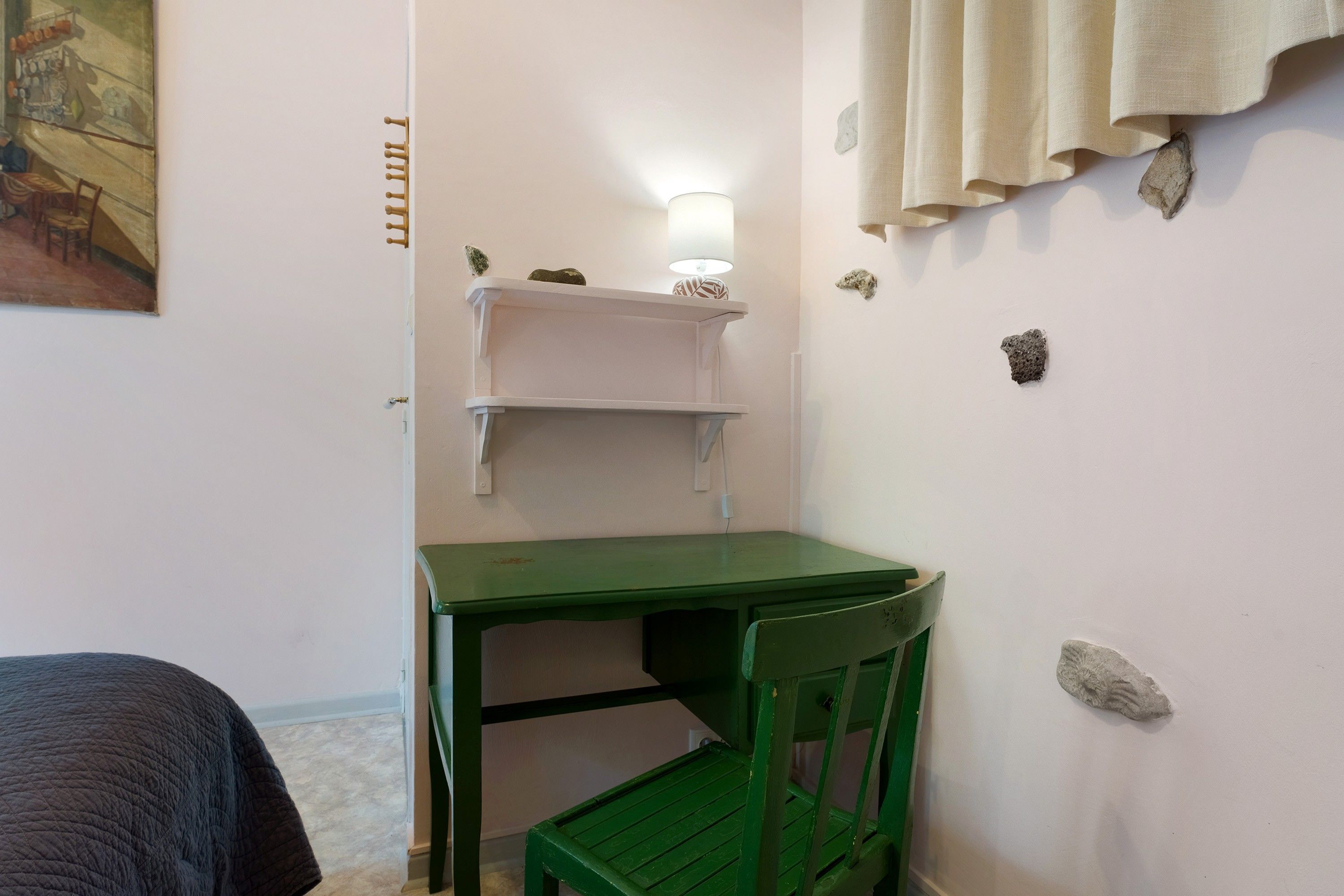 A small room with a green chair, a white shelf, and a bed.