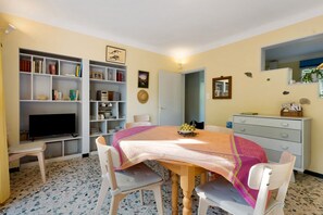 A dining area with a table set for four, surrounded by chairs, a television, and a bookshelf with various items.