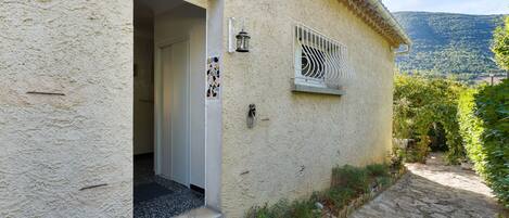 Un edificio rústico con una escalera de piedra que lleva a una puerta, una pequeña ventana con una reja de metal y vistas a un paisaje montañoso.