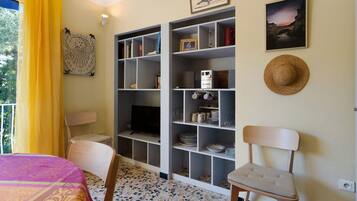 Ein Zimmer mit einem Bett, einem Sessel, einem Bücherregal und einem Fernseher.