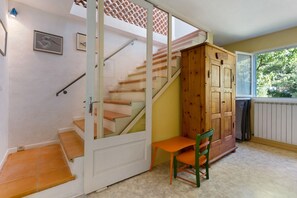 A room with a wooden staircase, a sliding door, a small table with a chair, and a window with a view of trees.