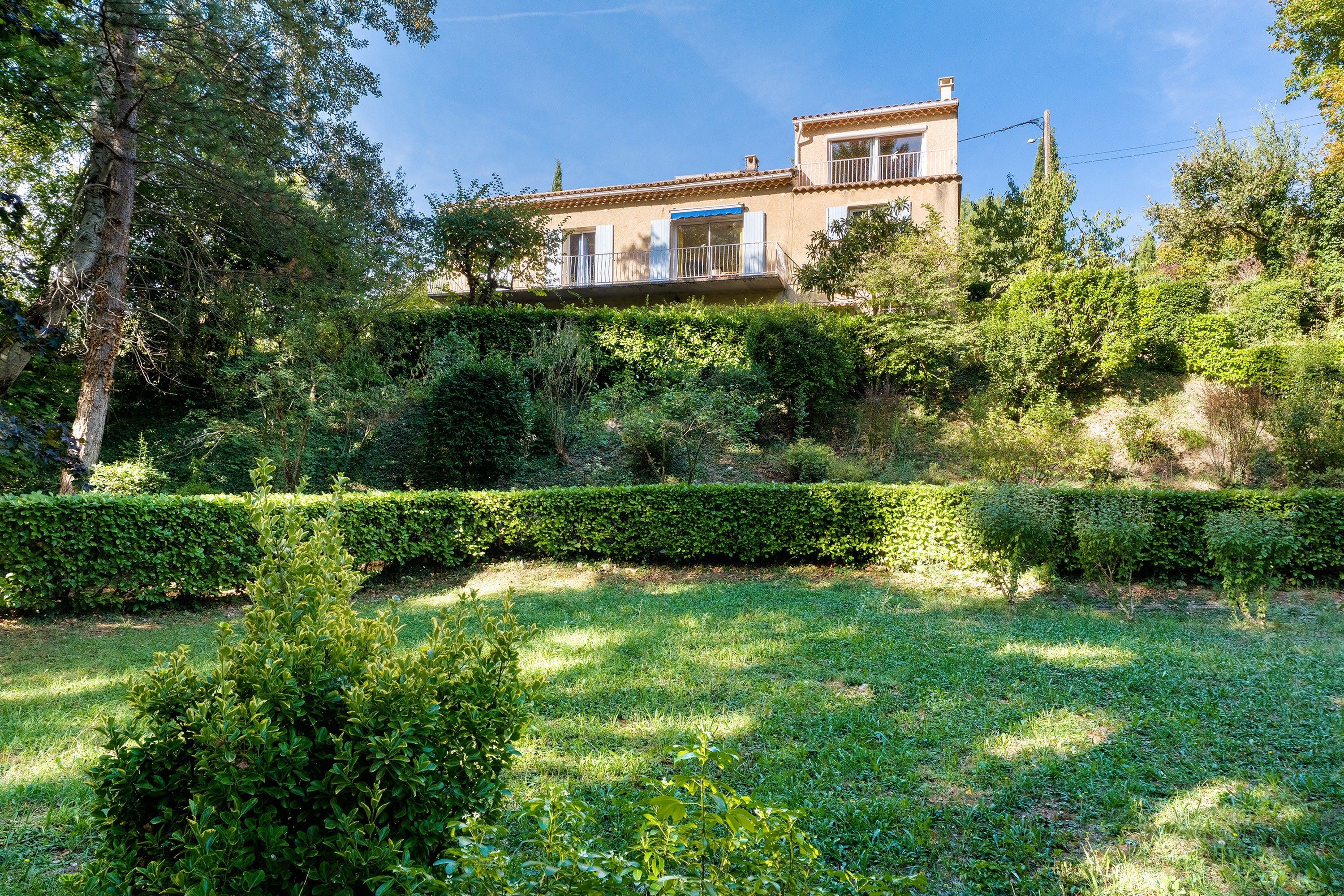 A residential building with a balcony, surrounded by well-maintained hedges and trees.