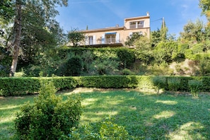 A residential building with a balcony, surrounded by well-maintained hedges and trees.