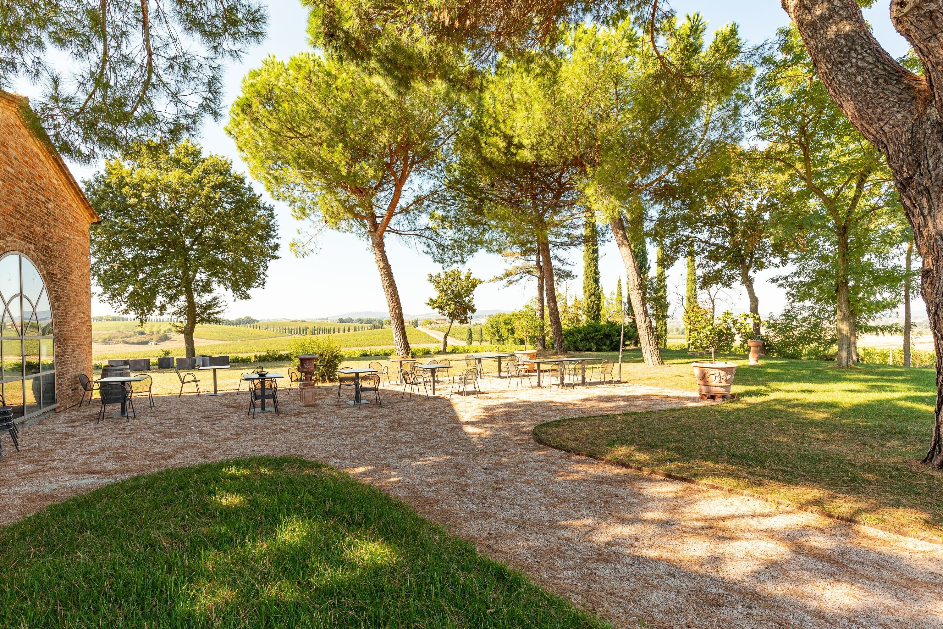 An outdoor seating area with tables and chairs, surrounded by trees and a view of the countryside.