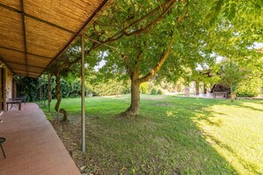 Un espacio al aire libre techado con patio de ladrillo, un árbol y zona de barbacoa.