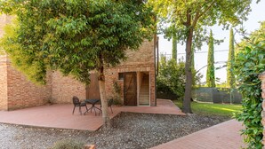 A brick building with a covered patio area, a table with chairs, and a small garden with gravel and plants.