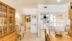 Un coin repas avec une table en bois, des chaises, un buffet aux portes vitrées et, au fond, une cuisine.