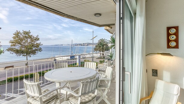 Un balcon avec une table ronde et des chaises, une vue sur la mer et une horloge au mur.