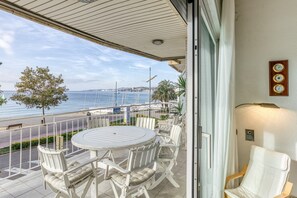 Un balcon avec une table ronde et des chaises, une vue sur la mer et une horloge au mur.