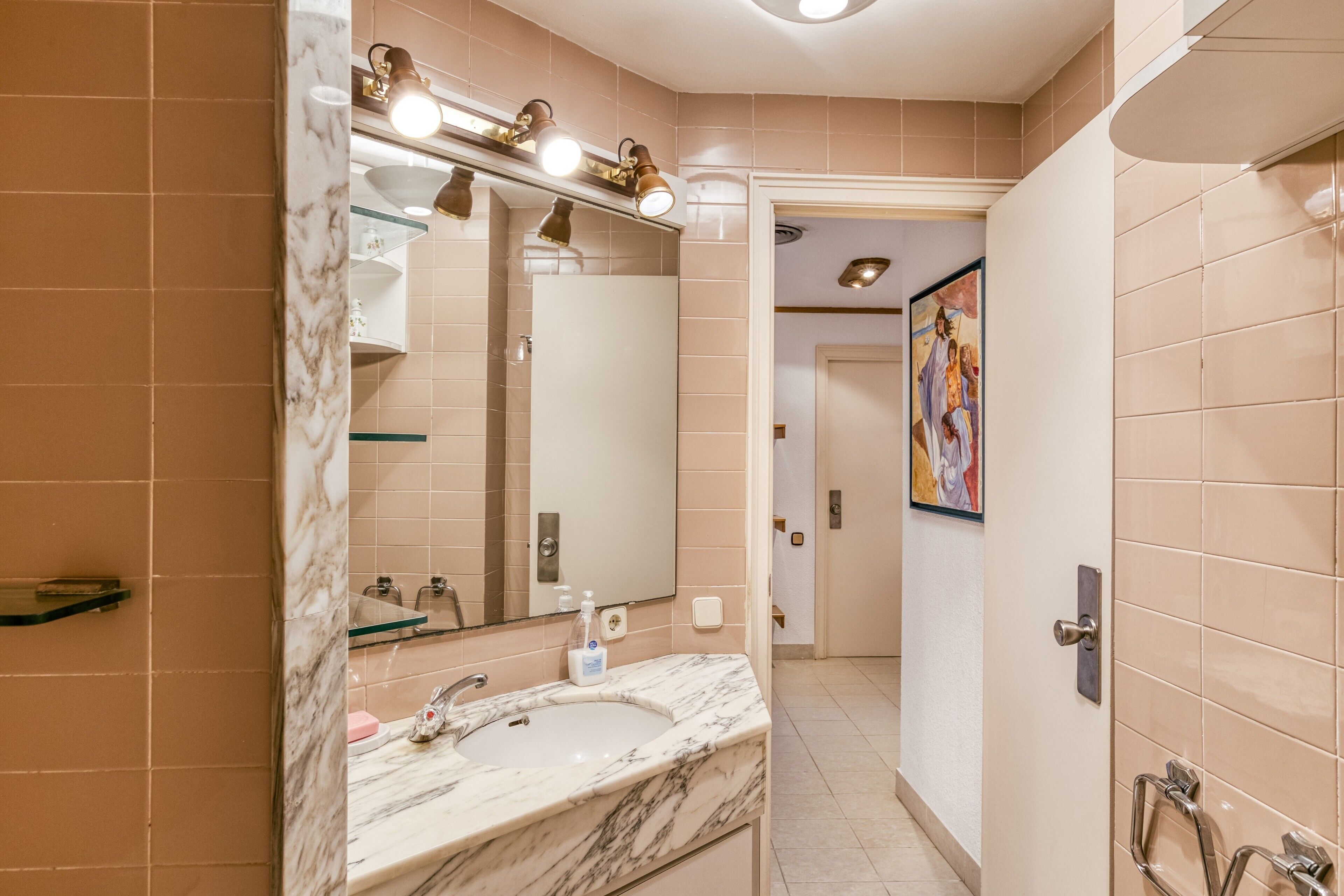 Une salle de bain avec un lavabo en marbre, un miroir avec éclairage intégré et un espace douche.