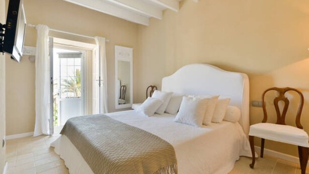 Une chambre à coucher comprenant un lit, une chaise, un téléviseur et une porte donnant sur l’extérieur.