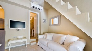 Un salon avec un canapé blanc, un téléviseur, une horloge et un escalier.