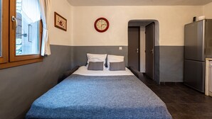 Quarto com cama, relógio, porta e frigorífico.