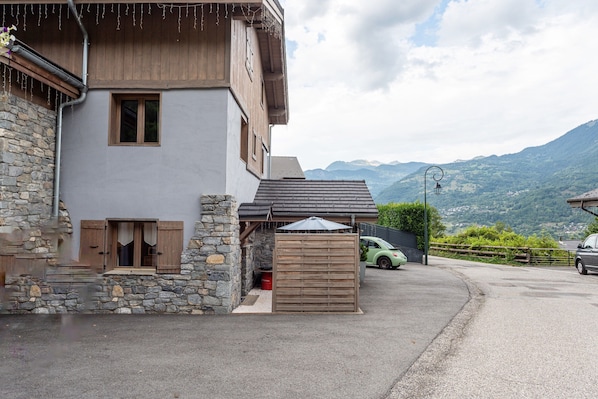 A two-story building with a stone facade, wooden shutters, and a car parked in front.