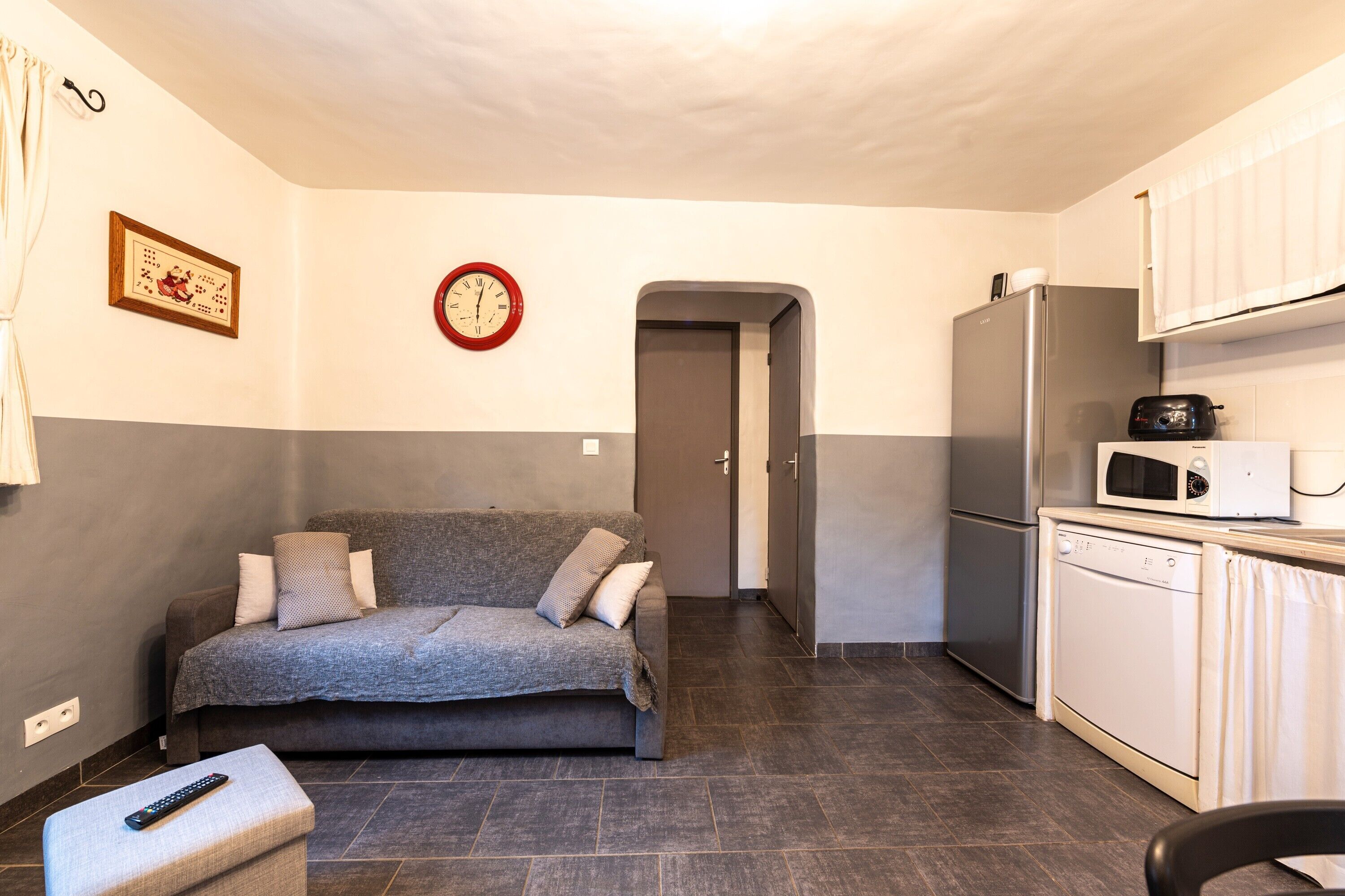 A compact living space with a sofa, a remote control, a microwave, and a refrigerator.