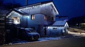 Uma casa com paredes de pedra, um carro estacionado na frente e luzes de fada.
