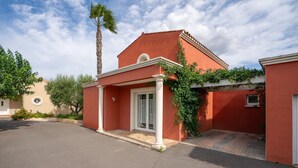 Un bâtiment rouge avec une porte blanche, un petit porche et un palmier.