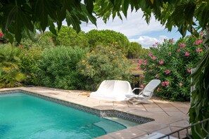 Ein Swimmingpool mit einer gefliesten Kante, umgeben von üppiger Vegetation und einem weißen Liegestuhl.
