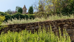 A stone wall with greenery in the foreground and a church with a bell tower in the background. - Holiday Home "Gîte Lou Barry" with Shared Pool & Wi-Fi (Mirabel-aux-Baronnies)