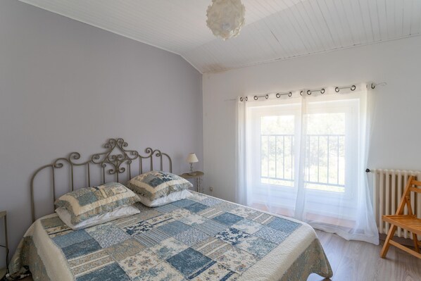 A bedroom with a bed, a chair, a window with curtains, and a radiator.