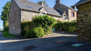 Une maison en pierre avec une allée en gravier, un petit jardin et une chaise bleue à l’extérieur.