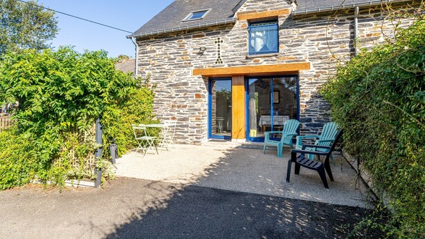 Une maison en pierre avec une porte en bois, une petite fenêtre et une terrasse en gravier aménagée avec des meubles d’extérieur.