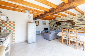 Una cocina con refrigerador, una mesa de comedor con sillas, un sofá y una pared de piedra.