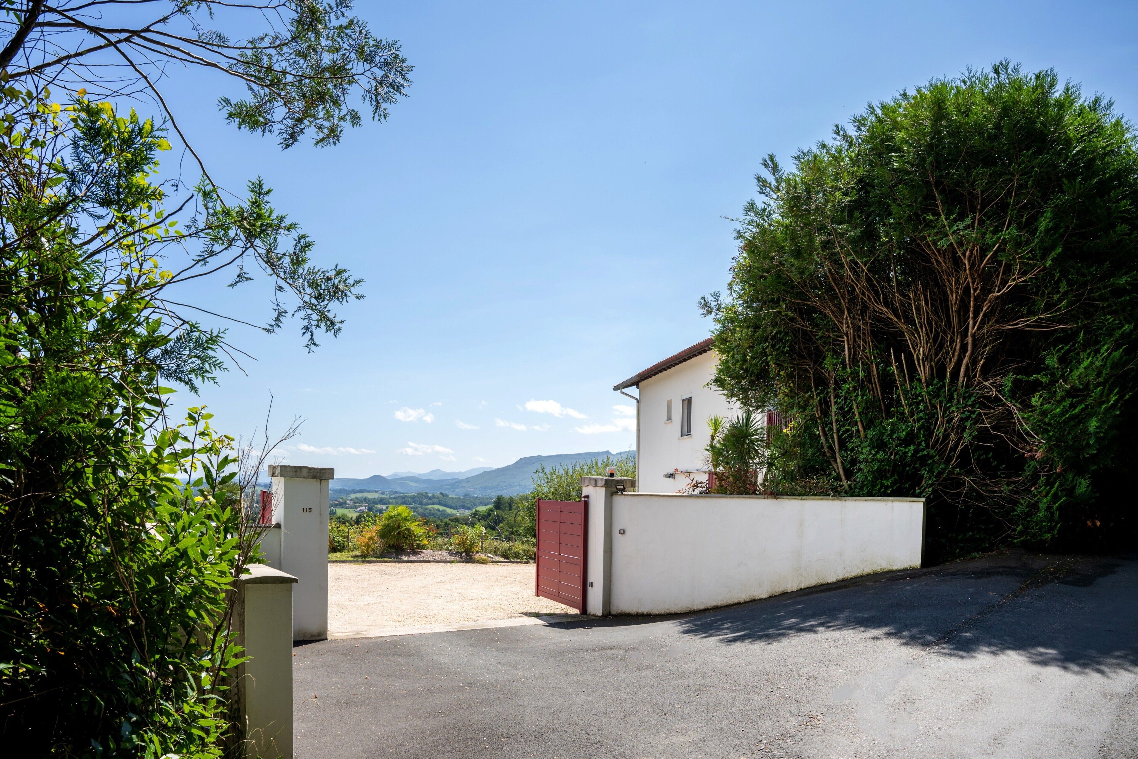 A gated property with a white building, a paved driveway, and a view of mountains.