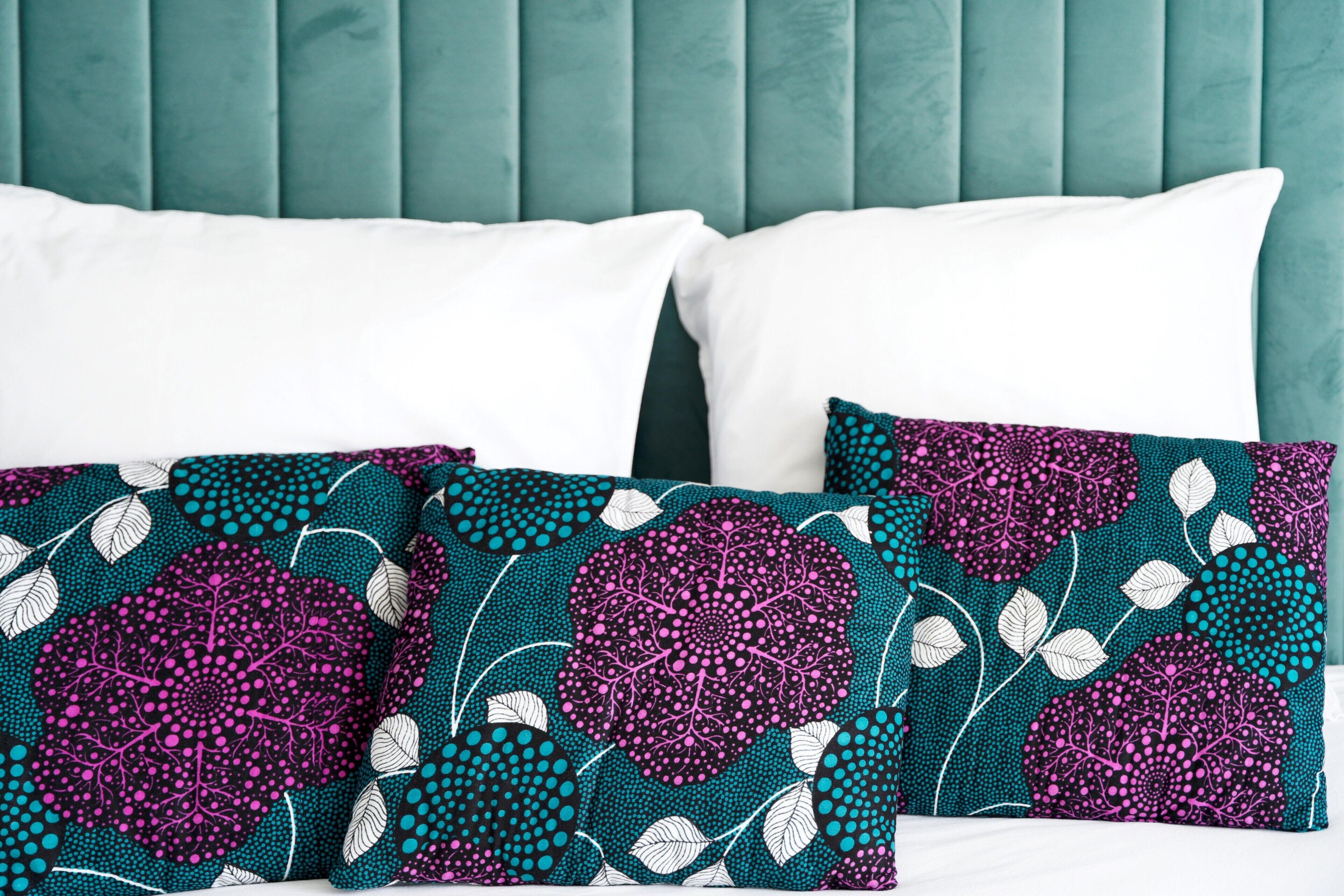 A bed with teal upholstered headboard, white and patterned pillows.
