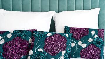 A bed with teal upholstered headboard, white and patterned pillows.