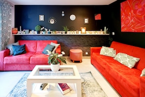 Una sala de estar con dos sofás rojos, una mesa de centro blanca y una pared de ladrillo negro decorativa.
